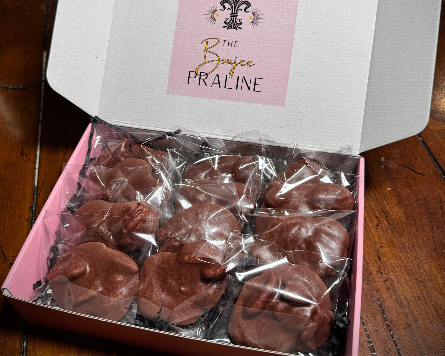 Box of chocolate pralines with 'The Boujee Praline' label on a wooden surface